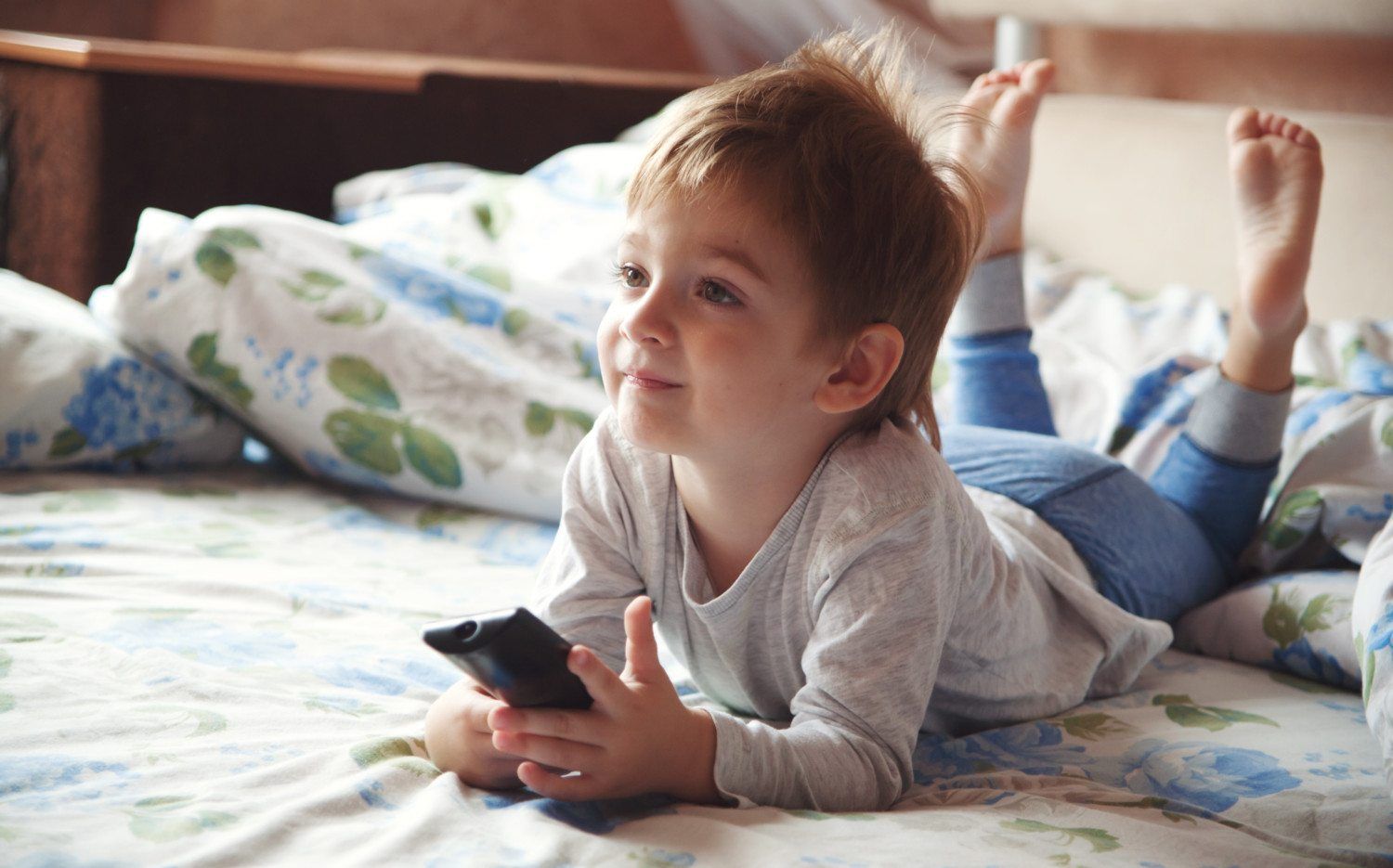 Child laying on bed holding TV remote