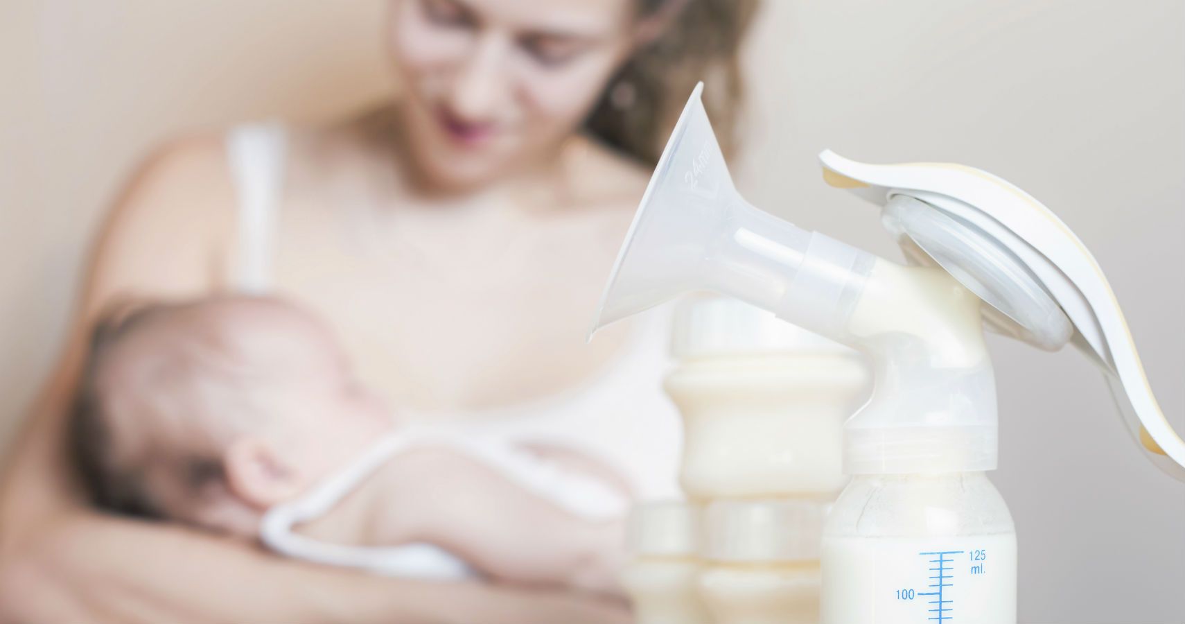 Mom holding baby with breast pump in the foreground