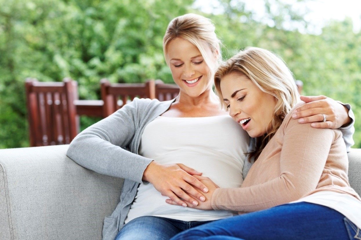 Lesbian couple touching pregnant partner's belly