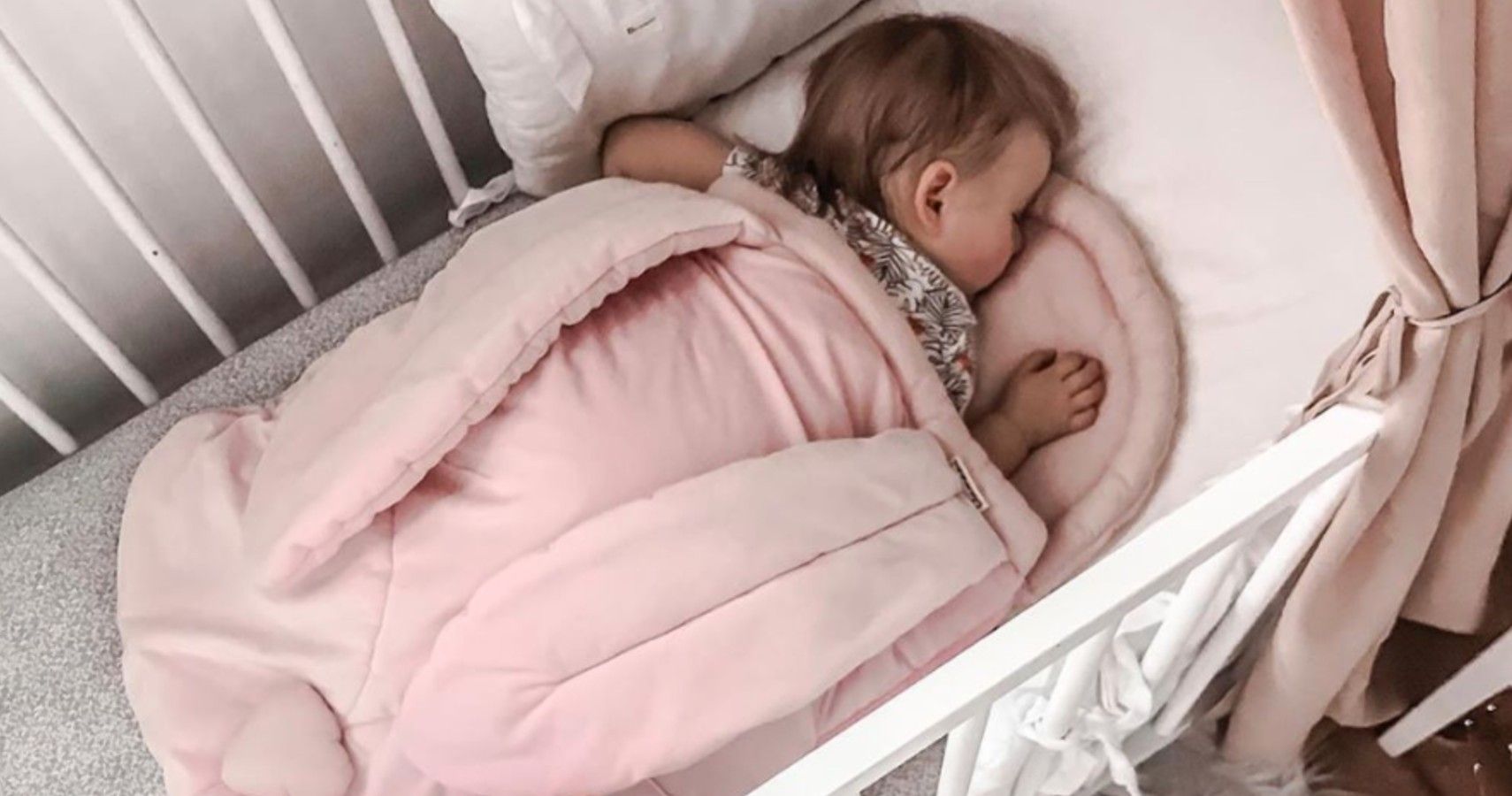 Baby sleeping in sleeping bag inside of a crib.