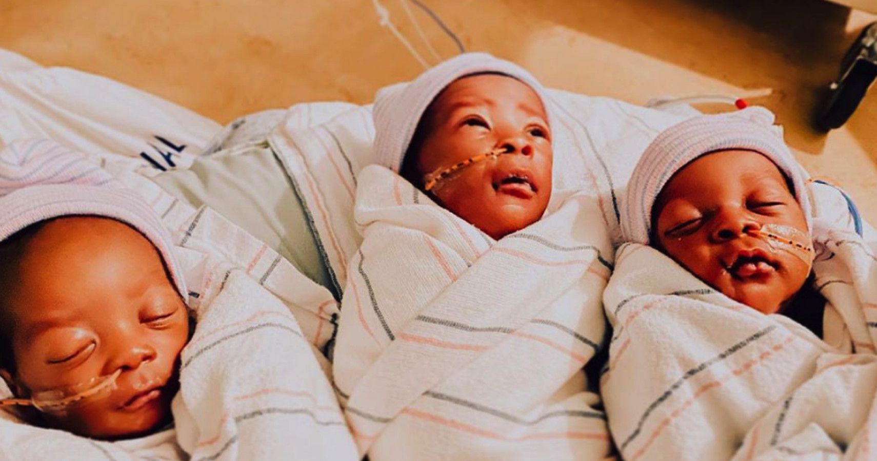 Infant triplets swaddled up with breathing tubes.
