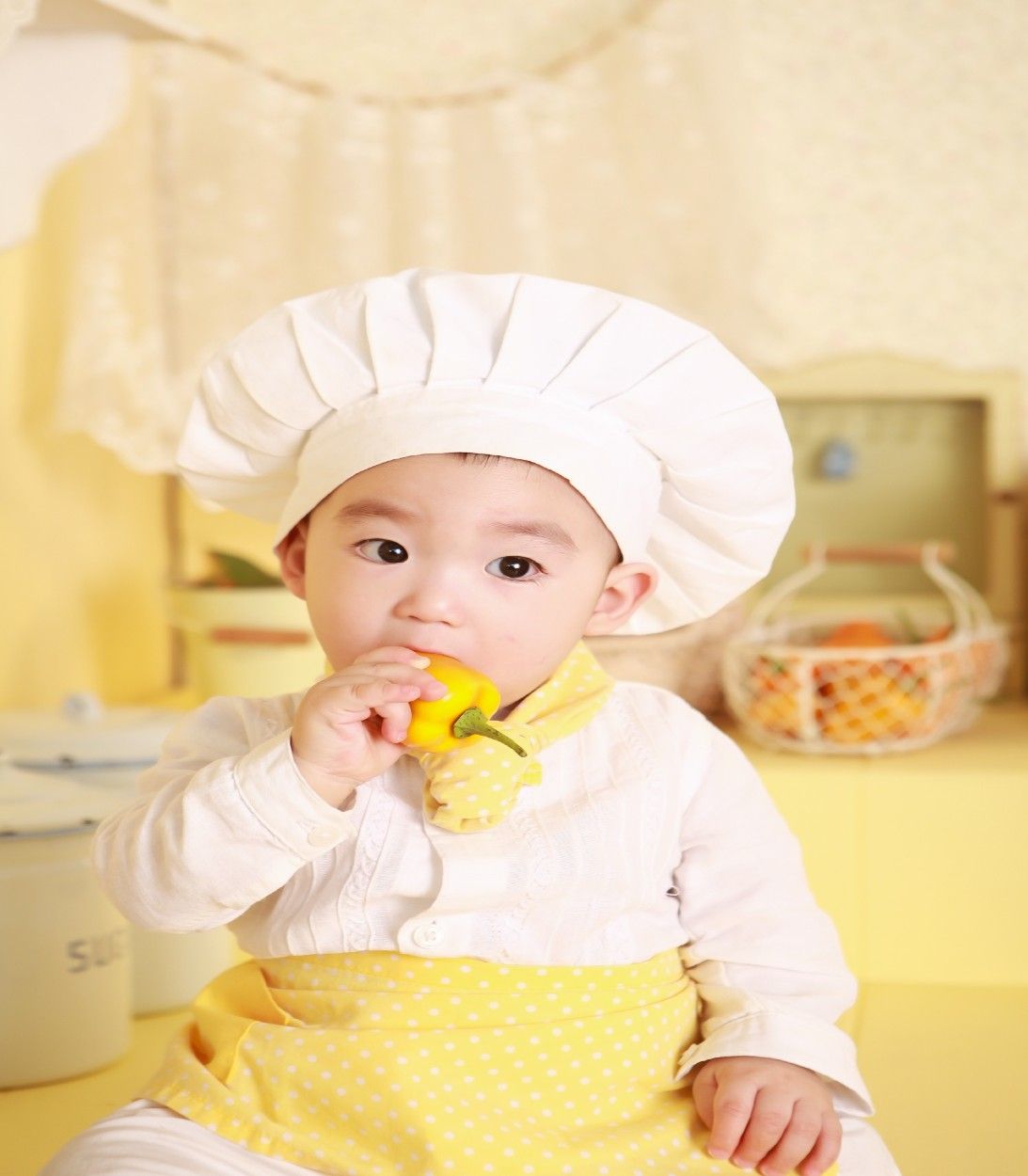 baby in a chef hat eating a yellow pepper
