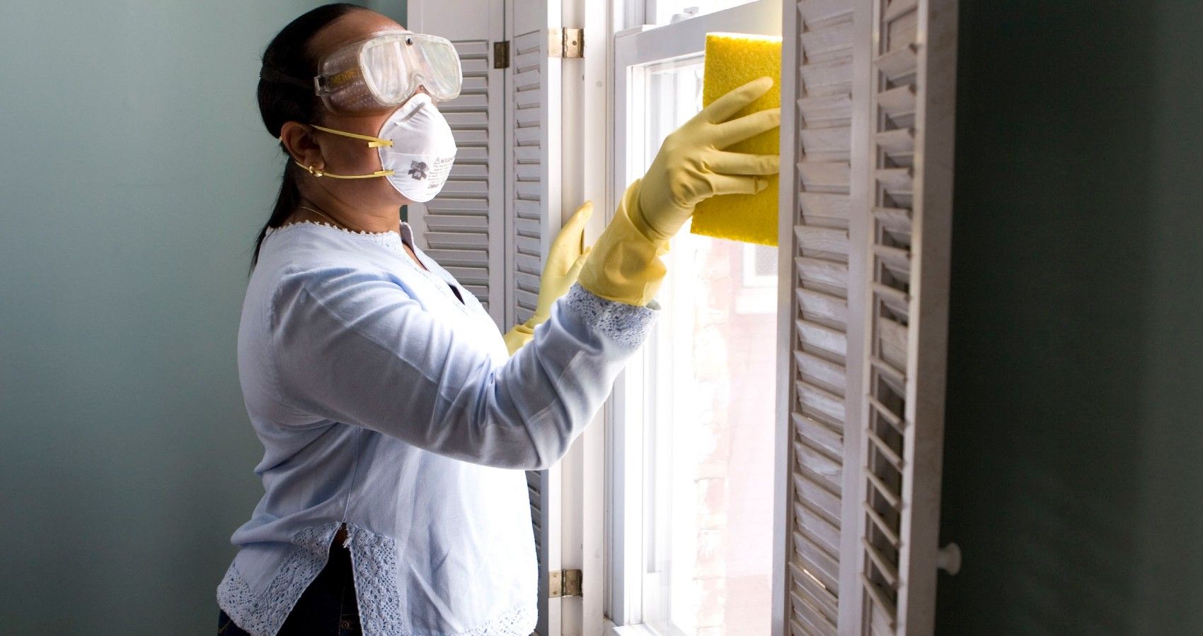 A pregnant woman cleaning a window with protective gear on