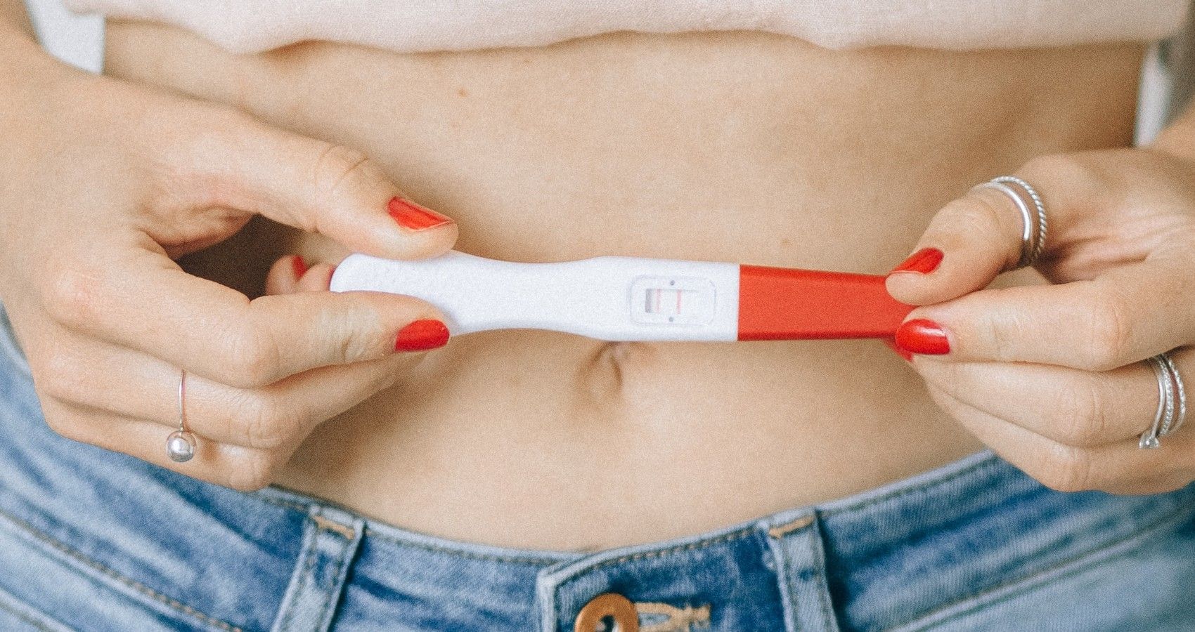 A woman holding a pregnancy test infront of her stomach