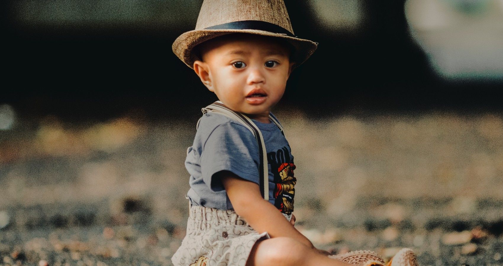 A toddler sitting outside with a hat on