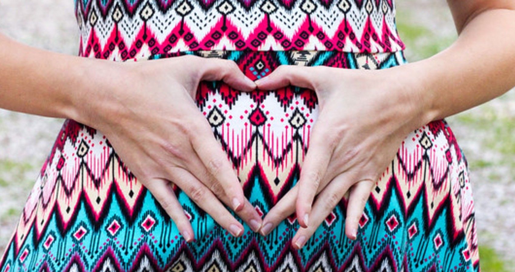 a woman holding her hands in a heart over her pregnancy bump