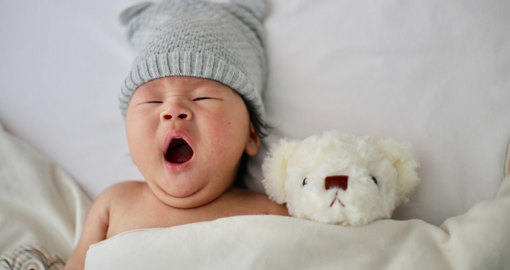 A Baby Yawning With A Stuffed Bear