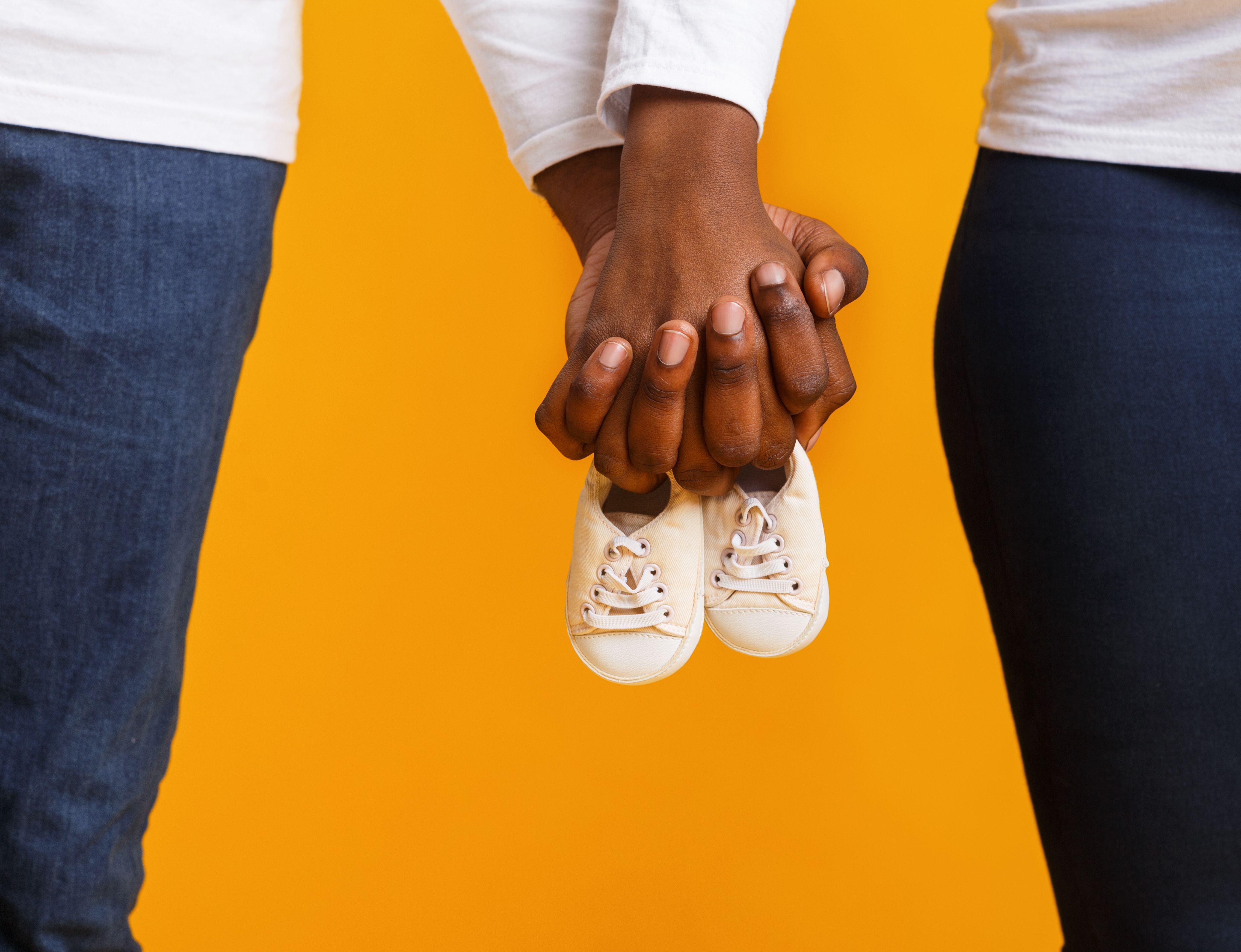 Black couple holding hands with baby shoes