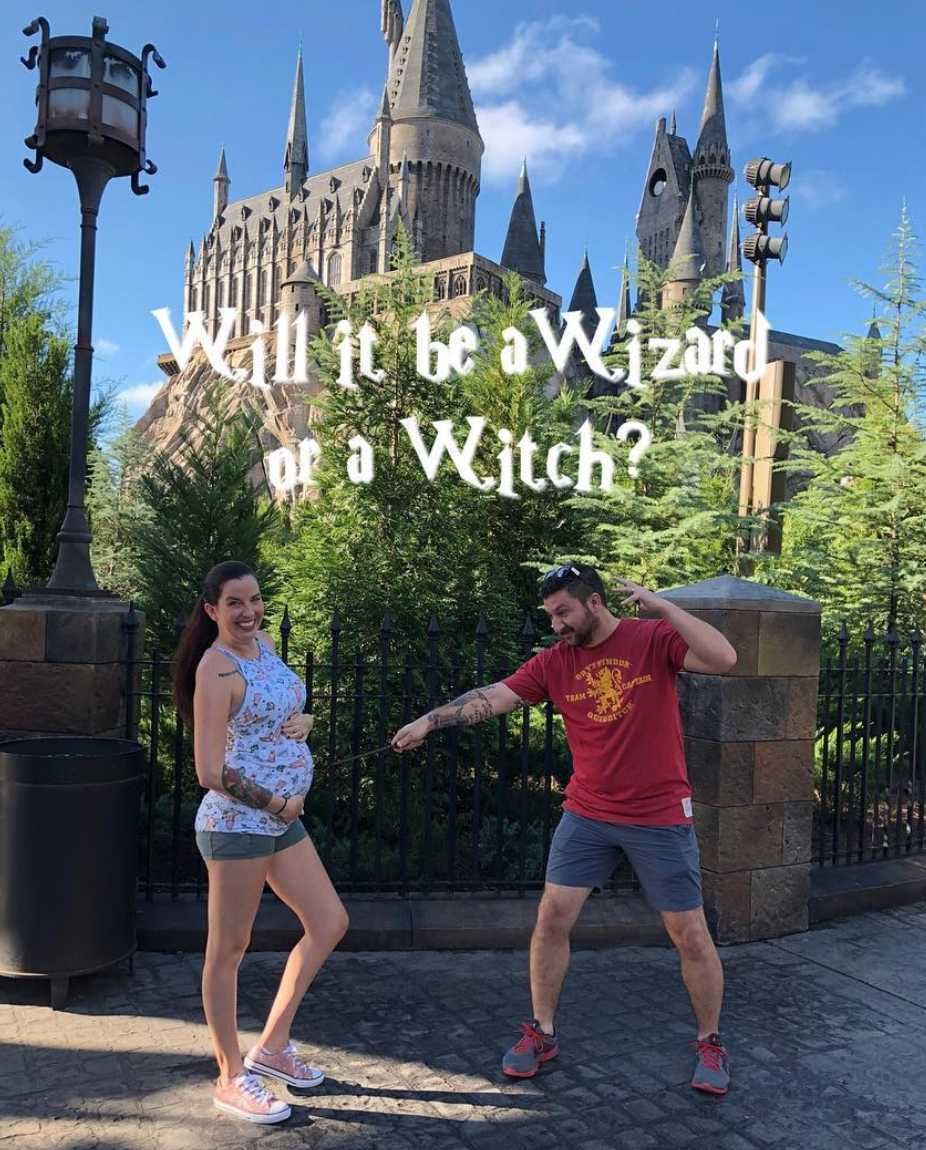 Couple standing in front of Hogwarts Castle pointing a wand at woman's pregnant belly